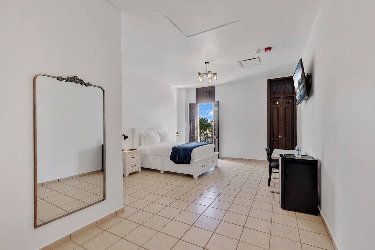Une chambre à coucher comprenant un lit, des tables de chevet, un miroir, une télévision et un petit meuble.