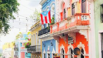 A street lined with colorful buildings, parked cars, and a pedestrian.