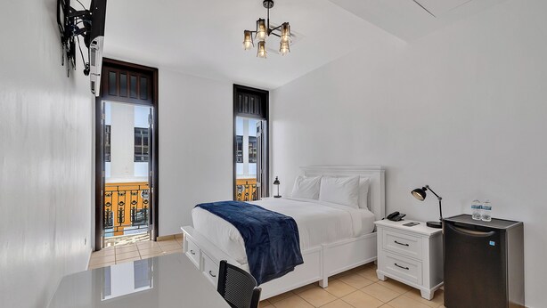 Ein modernes Hotelzimmer mit Bett, Nachttisch, Schreibtisch und kleinem Kühlschrank.
