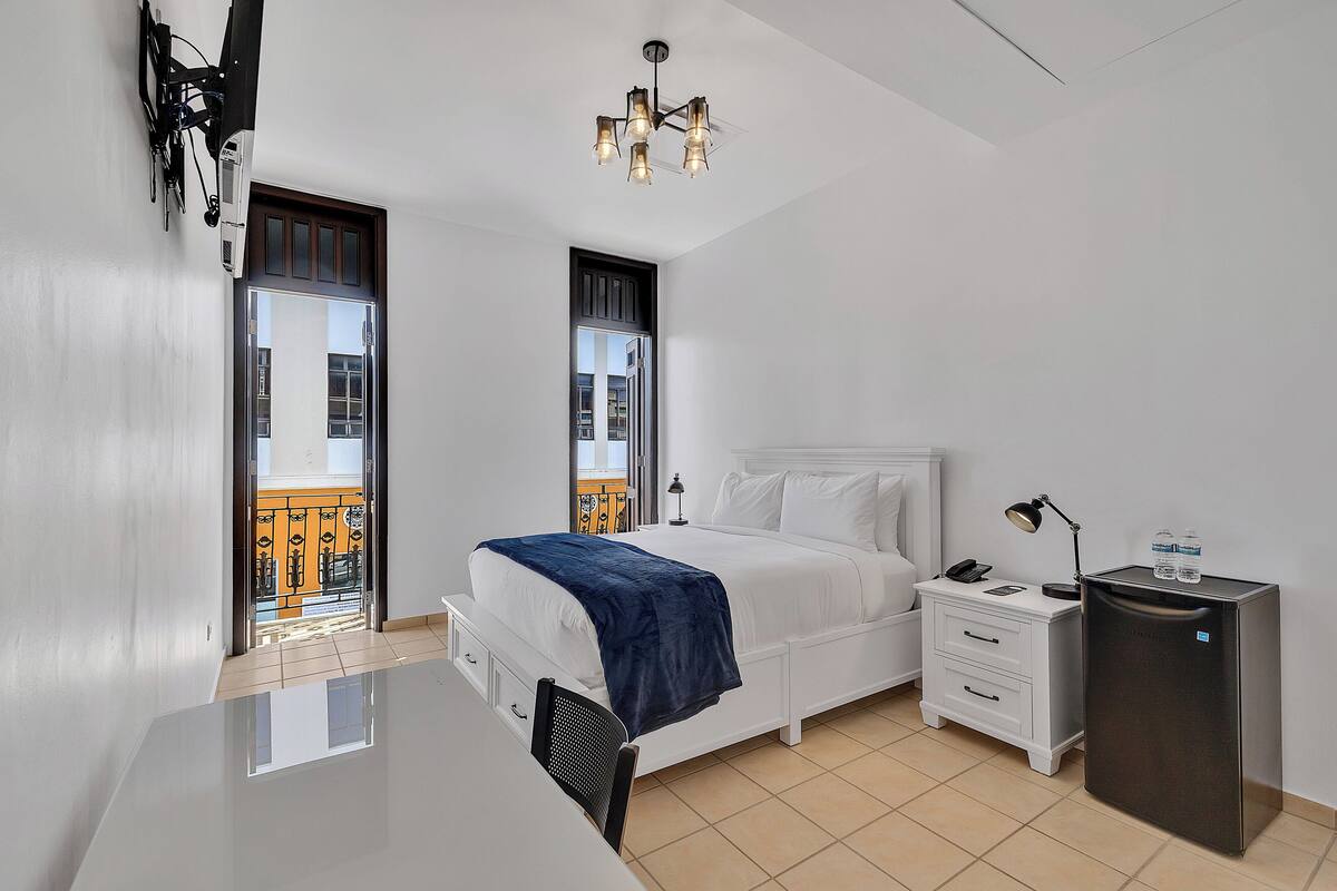 Une chambre d’hôtel moderne équipée d’un lit, d’une table de chevet, d’un bureau et d’un petit réfrigérateur.