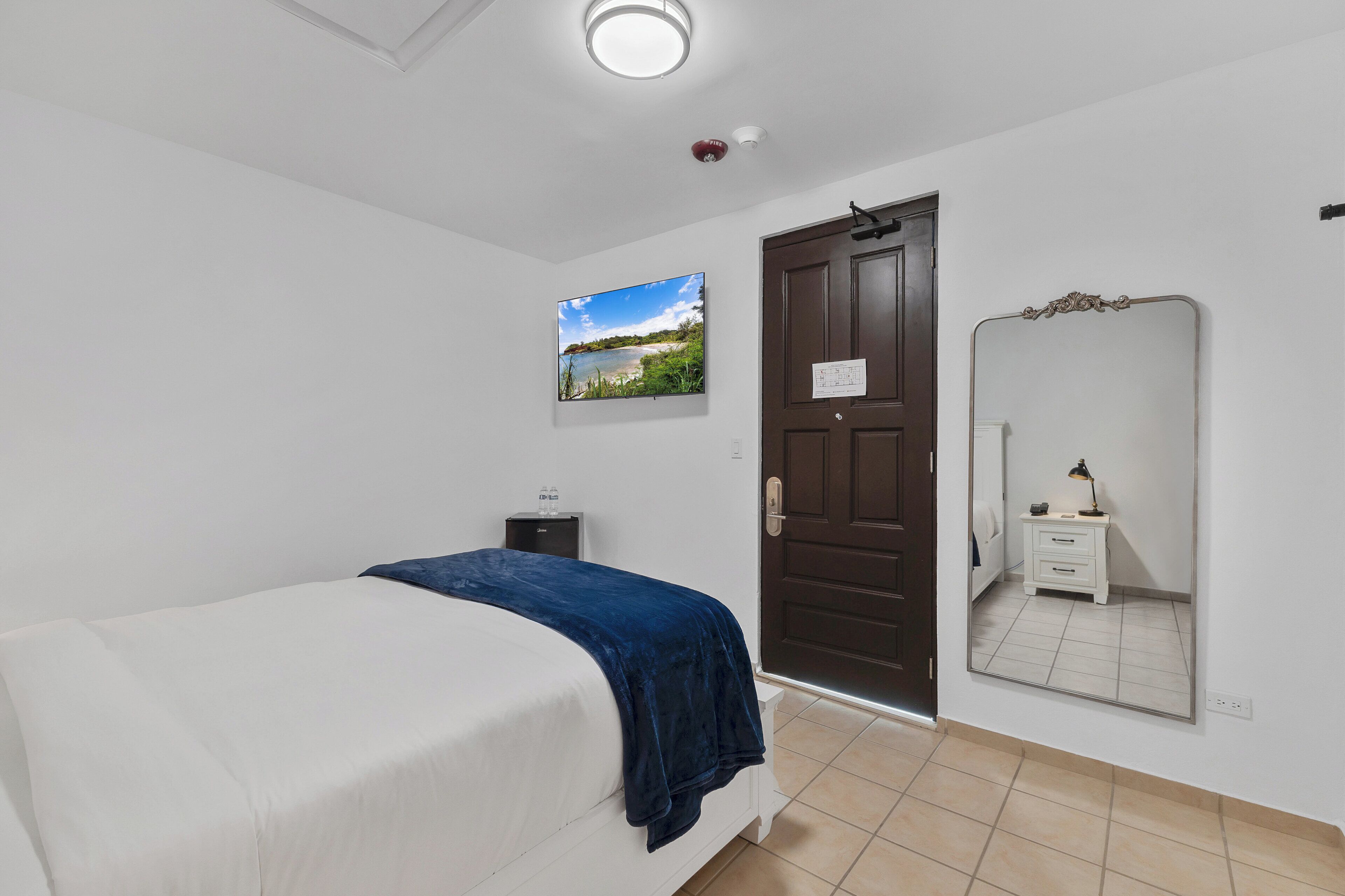 A bedroom with a bed, a nightstand, a mirror, and a door.