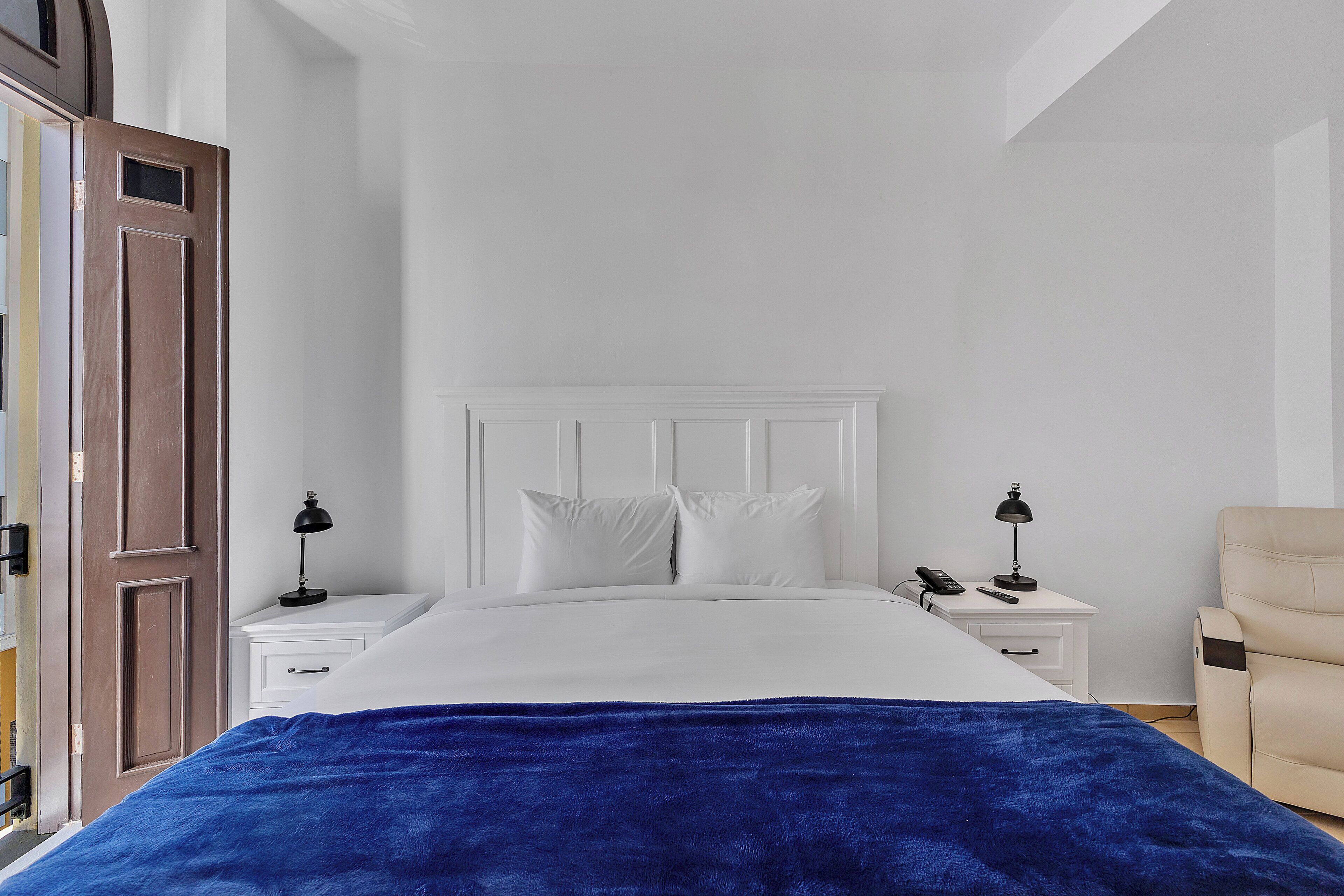 A bedroom with a bed, two bedside tables, a chair, and a wooden door.