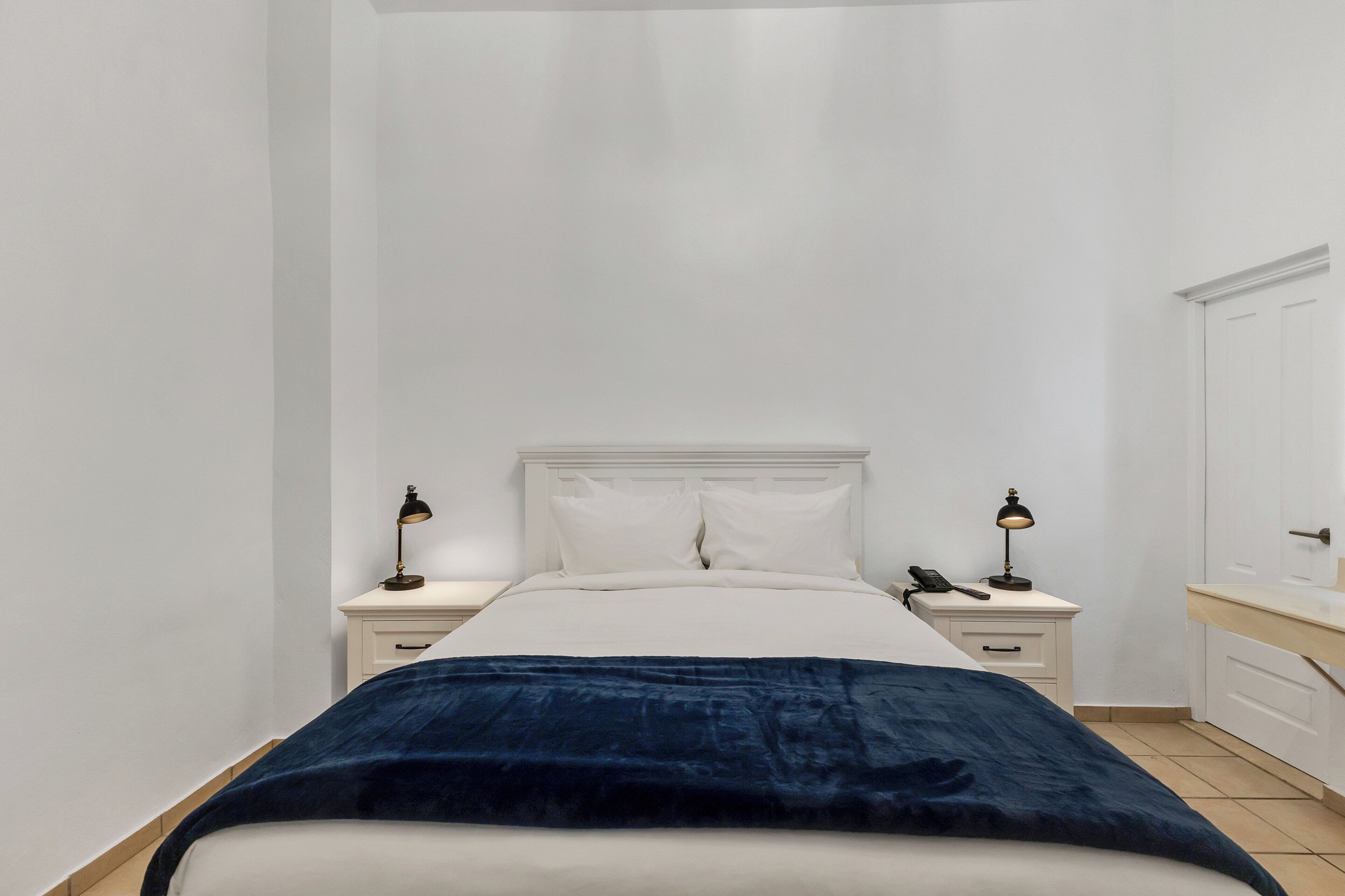 Un dormitorio con cama, dos mesitas de noche, una mesilla auxiliar, lámpara y espejo.