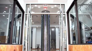 Eine Lobby mit Glastür, einer zentralen Dekorationssäule und einem kleinen Tisch mit Stühlen.
