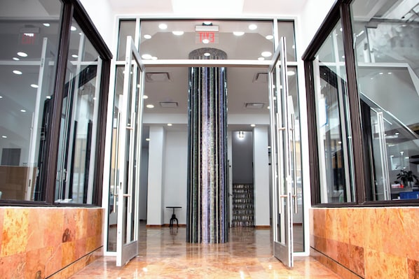 Un vestíbulo con puerta de vidrio, una columna decorativa central y una pequeña mesa con sillas.