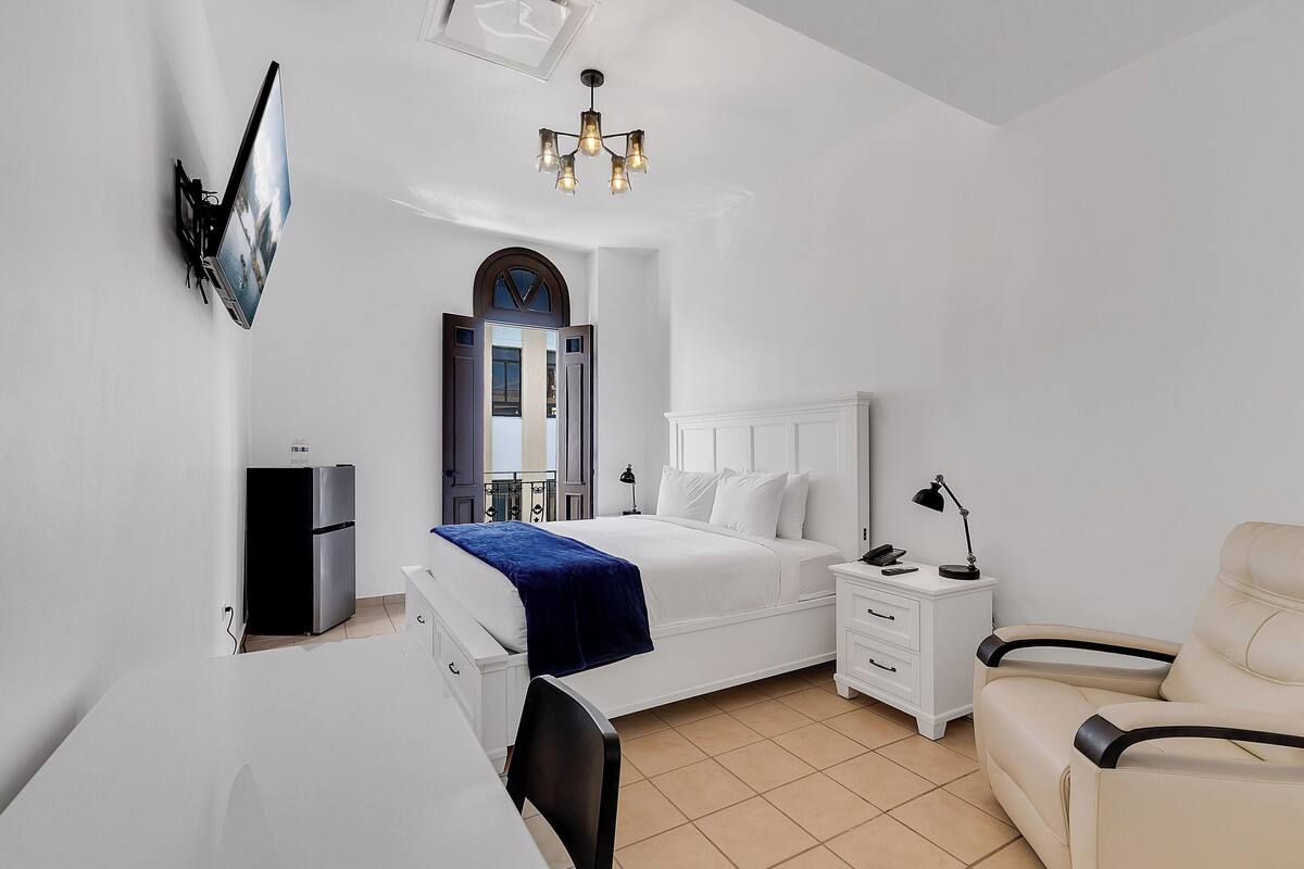 Une chambre d’hôtel moderne équipée d’un lit, d’une table de chevet, d’une chaise, d’un bureau et d’un téléviseur fixé au mur.