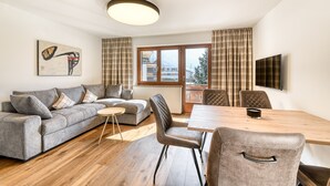 A modern living room with a grey sofa, a wooden dining table, and a TV mounted on the wall.