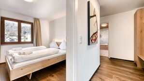 A modern hotel room with a wooden bed, a large window with curtains, a painting on the wall, and a wooden floor.