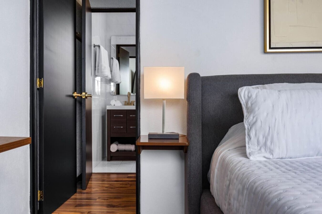 A hotel room with a bed, a bedside table with a lamp, a wardrobe, and a mirror.