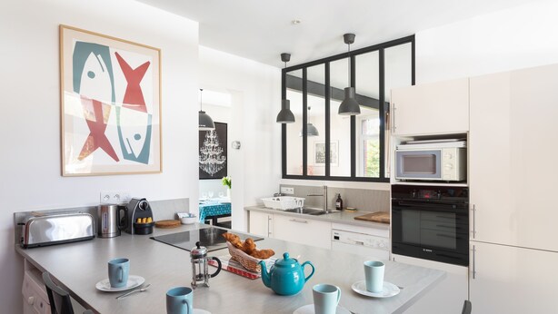 Una cocina moderna con armarios blancos, un tostador de acero inoxidable, una tetera y una tetera azul sobre la isla.