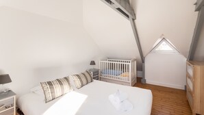 Un dormitorio con una cama grande, una cuna, una mesita de noche y un aparador de madera.