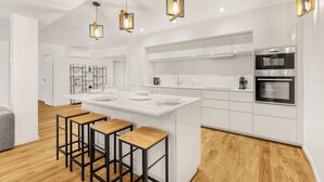 Een moderne keuken met witte kastjes, een centraal eiland met krukken en roestvrijstalen apparatuur.