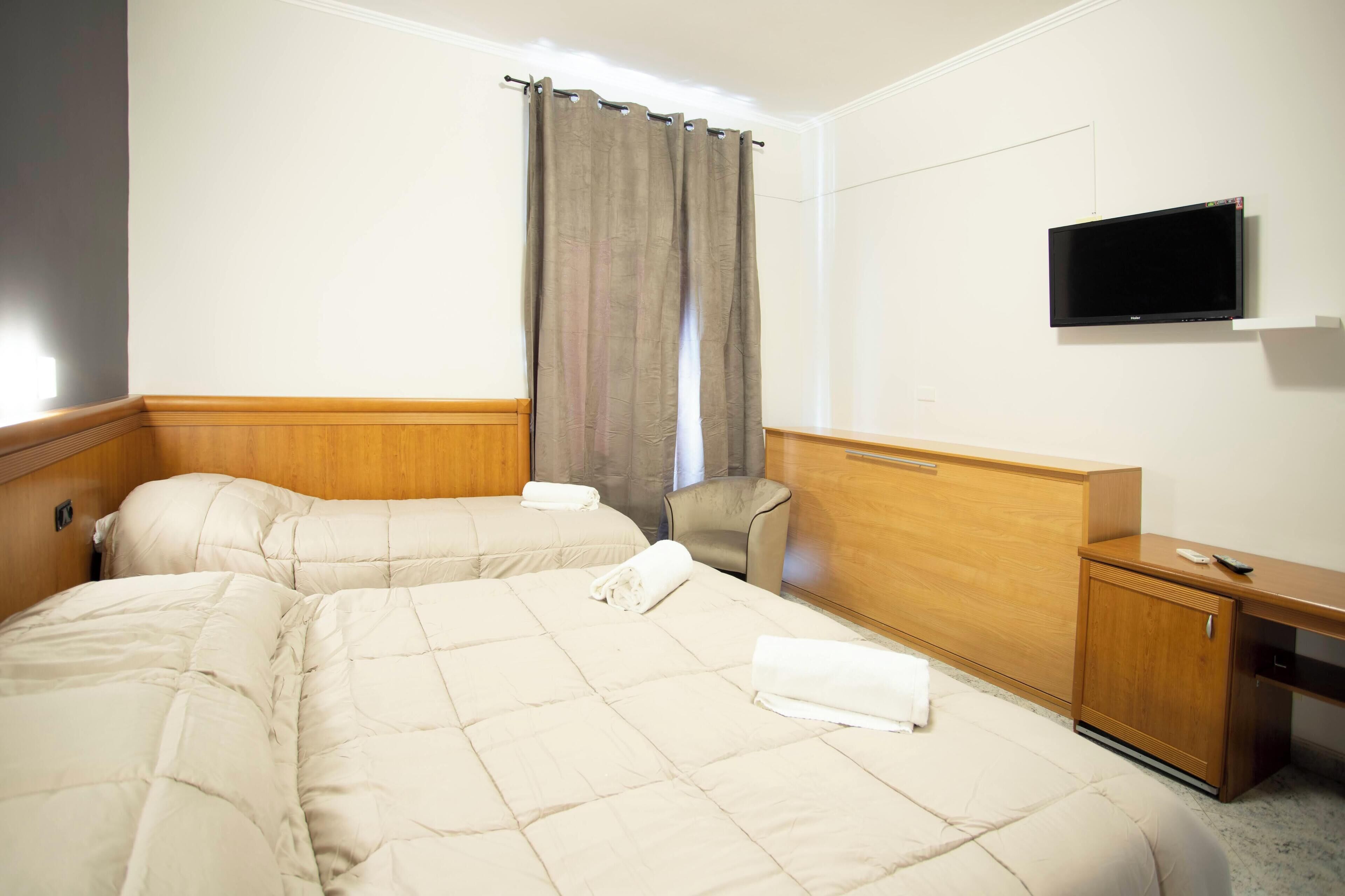 A hotel room with two beds, a TV mounted on the wall, a wooden desk, and a chair.