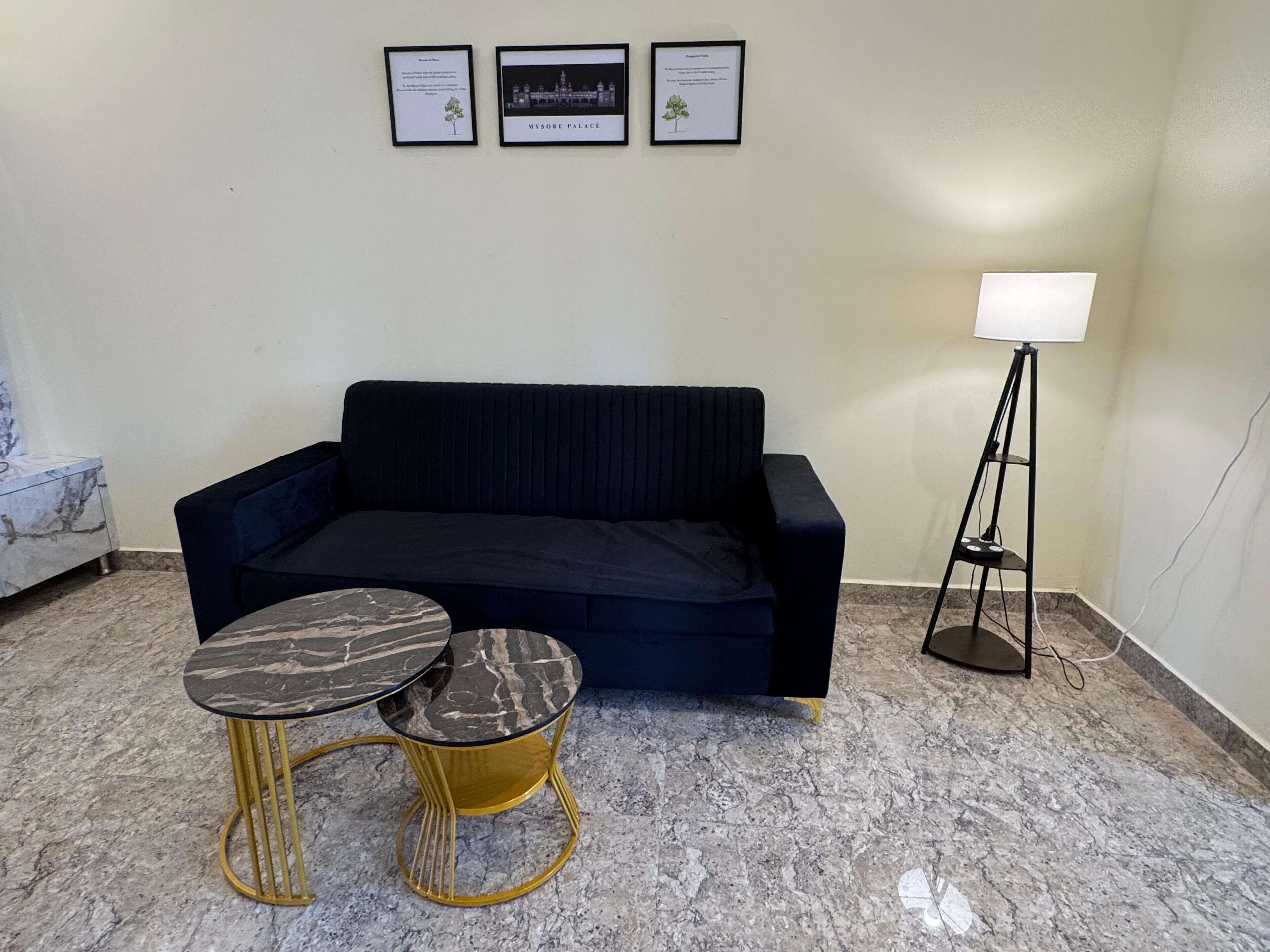 Ein dunkelblaues Sofa, zwei gold- und schwarz marmorierte Tische, eine Stehlampe und drei gerahmte Bilder an der Wand.