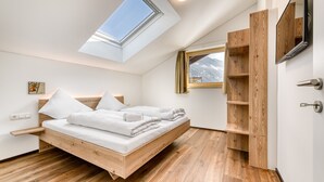 A modern bedroom with a skylight, wooden bed frame, and built-in wooden shelving. - Alpenblick Appartements - 3-zimmer Dachgeschoss (Schruns)