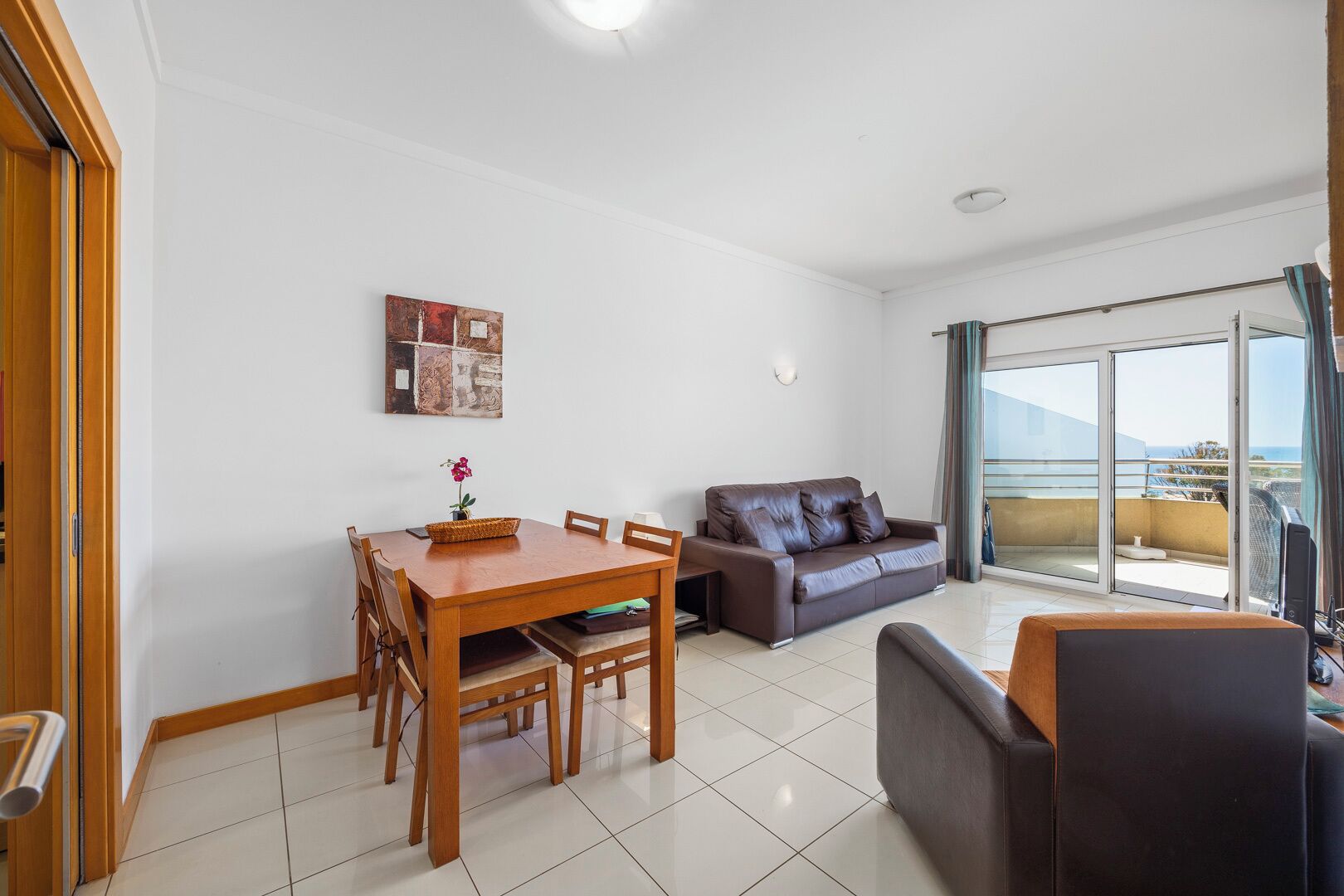 A modern living room with a dining table, a sofa, and a balcony with a view.