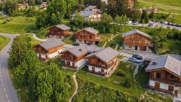 Un grupo de chalets de madera con balcones, rodeados de abundante vegetación y una carretera.