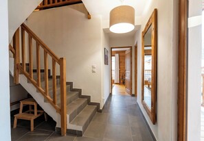 Un escalier avec des rampes en bois menant à un palier, un couloir avec un luminaire, et une vue sur une chambre à coucher avec un lit et des rideaux.
