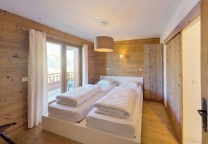 Une chambre avec deux lits, des murs en bois, une fenêtre avec des rideaux et une lampe suspendue.