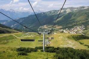 A mountain landscape with a ski lift, green fields, and distant houses.