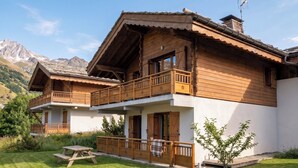 Un chalet con balcón, terraza de madera y montañas al fondo.