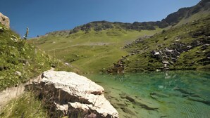 Un lago de montaña cristalino con costas rocosas y un sendero que lo atraviesa.