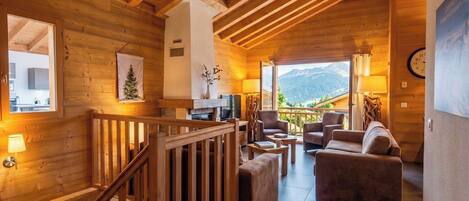 A wooden interior with a staircase, a seating area with a view of mountains, and a clock on the wall.