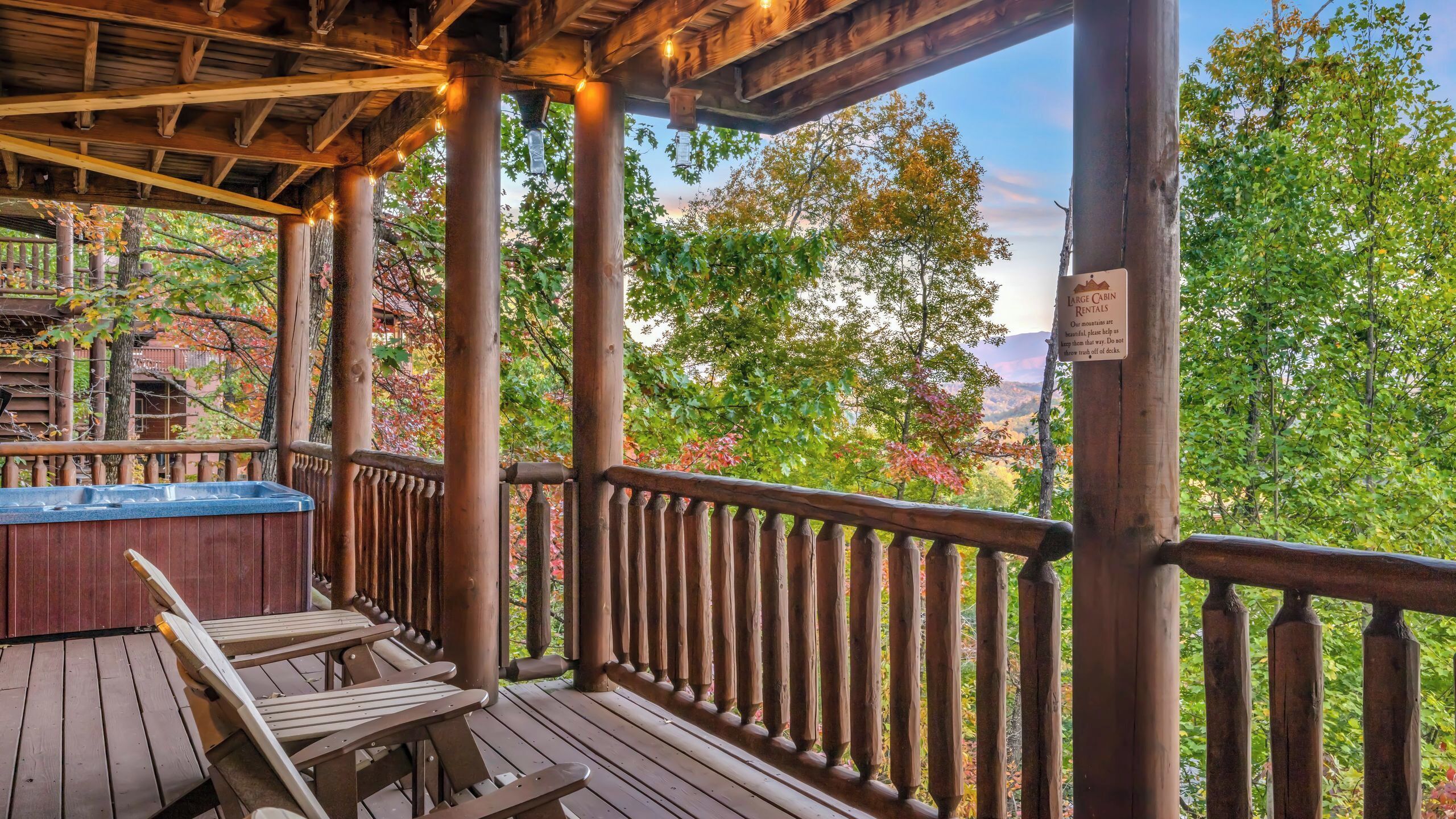 Une terrasse en bois avec un jacuzzi, des chaises en bois et une vue sur les arbres et les montagnes.