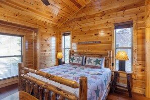 A wooden cabin bedroom with a bed, two bedside lamps, and a window with blinds.