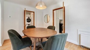 Ein runder Holztisch mit vier Stühlen, eine Pendelleuchte, eine Waschmaschine und ein Spiegel an der Wand.