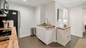 Eine moderne Küche mit weißen Schränken, einem Edelstahl-Kühlschrank, einer Spüle mit Holz Arbeitsplatte und einer kleinen Mülltonne.
