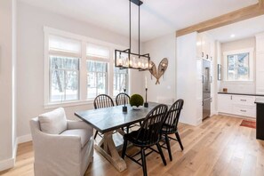 A dining area with a wooden table, black chairs, a white sofa, and a modern chandelier.