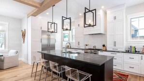 Een moderne keuken met witte kasten, een groot keukenblok met barkrukken en hanglampen.