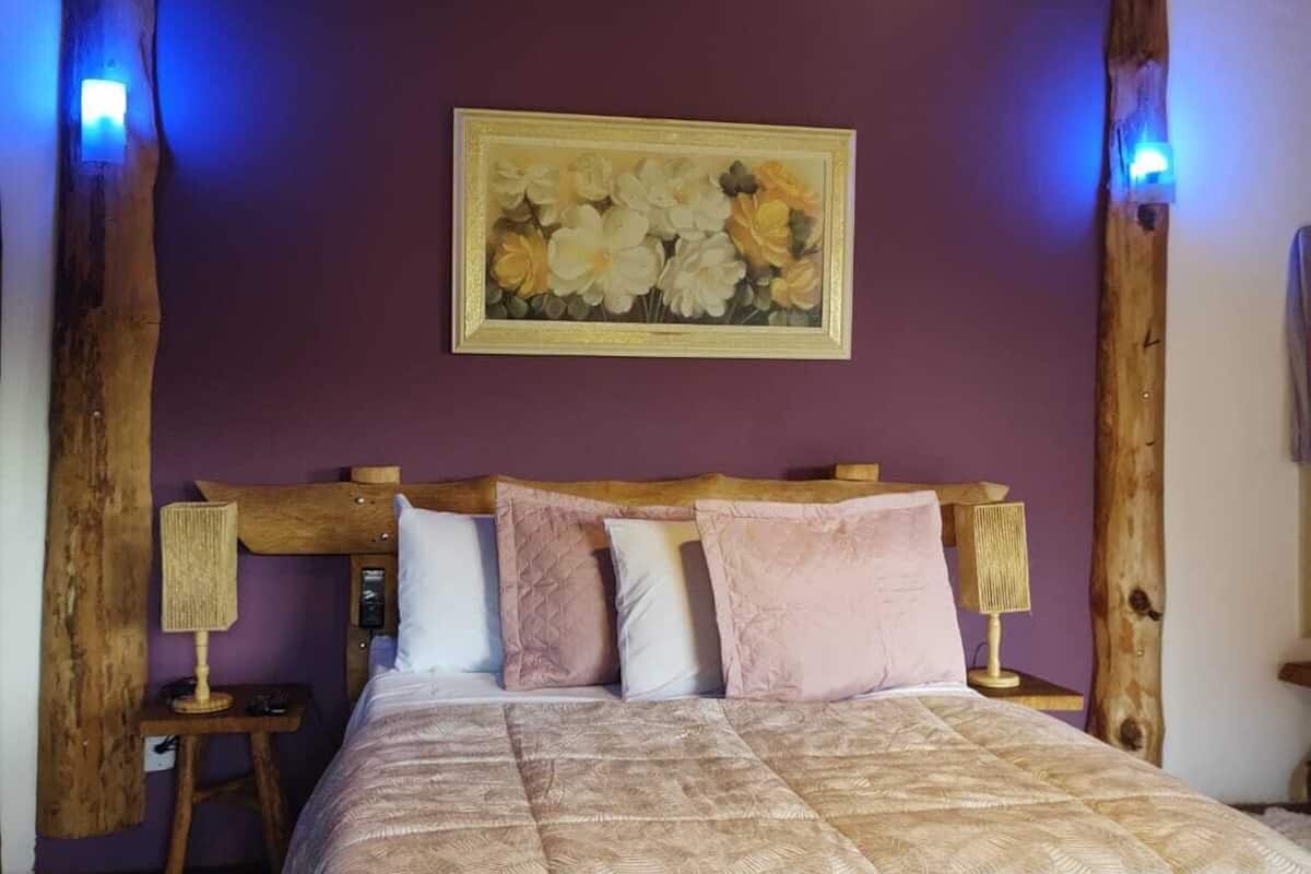 A bedroom with a wooden headboard, a large bed with a patterned bedspread, two bedside lamps, and a wall-mounted painting.