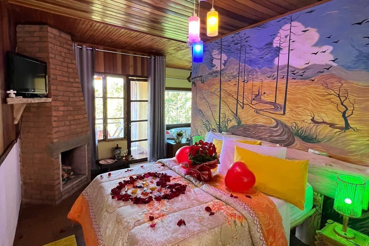 A cozy room with a bed, a fireplace, a mural, and a television.
