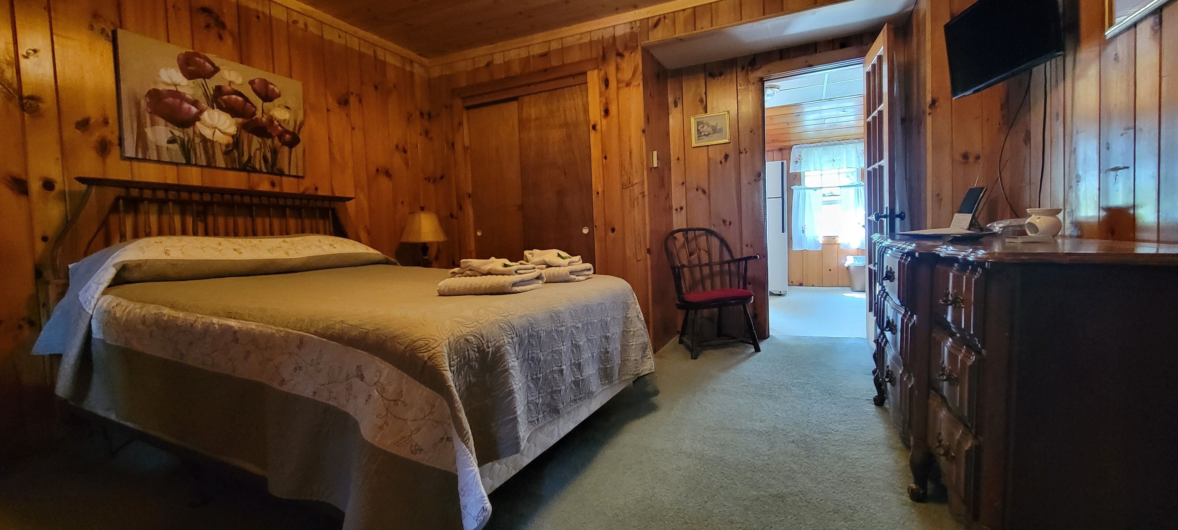 Um quarto com painéis de madeira, com uma cama, uma cadeira, uma cômoda e um quadro na parede.