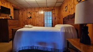 Una stanza con rivestimento in legno, un letto, una cassettiera, una TV e una lampada.