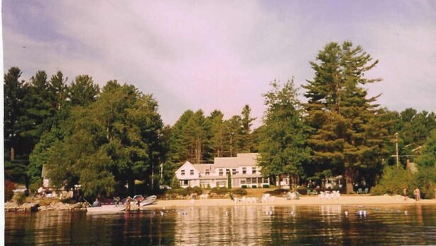 Una proprietà sul lago con una casa grande, immersa tra alberi fitti e un’acqua calma.