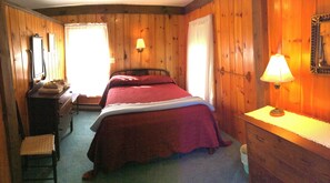 Ein Zimmer mit Holzboden, einem Bett, einem Schrank, einem Sessel und einer Lampe.