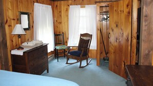 Una stanza con rivestimenti in legno, un letto, una cassettiera, una poltrona a dondolo e uno specchio.