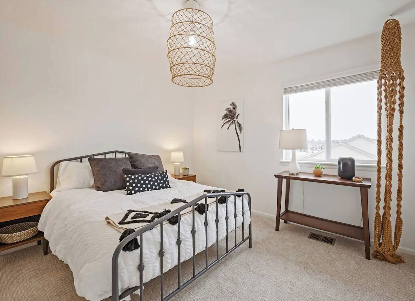 A bedroom with a bed, bedside tables, a desk, a window, and a hanging light fixture.