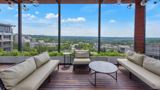 An outdoor deck with a wooden ceiling, a sofa, a round table, and a view of a cityscape. - The Art of Luxury Living  Heart of Sandton (Johannesburg)