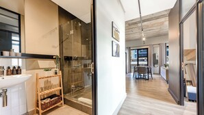 A modern bathroom with a glass shower, a wooden shelf with toiletries, and a sink. - The Art of Luxury Living  Heart of Sandton (Johannesburg)