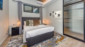 A modern bedroom with a large bed, a nightstand, a bedside table, a window with curtains, and a wall-mounted air conditioner. - The Art of Luxury Living  Heart of Sandton (Johannesburg)