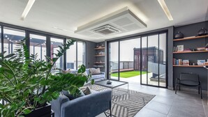 A modern living room with a sofa, coffee table, and potted plants. There are large windows and a view of the outside. - The Art of Luxury Living  Heart of Sandton (Johannesburg)