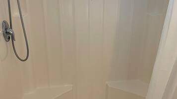 A white shower enclosure with a handheld showerhead and a fixed showerhead, a drain in the center, and a towel rack on the wall.
