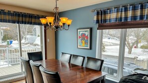 Comedor con una mesa y sillas de madera, una araña, un ventanal con vistas al exterior y un cuadro en la pared.