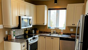 Una cocina con gabinetes blancos, microondas, estufa y refrigerador.