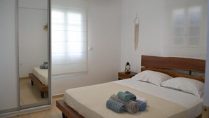 Une chambre à coucher comprenant un lit, une table de chevet, une lampe, un miroir et une fenêtre avec des stores.