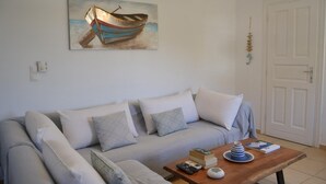 Un salon avec un canapé, une table basse, un tableau représentant un bateau et une porte.